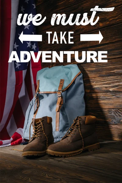 Botas de trekking, mochila y bandera americana en superficie de madera con debemos tomar ilustración aventura - foto de stock