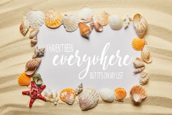 Frame of seashells near placard with I have not been everywhere, but it is on my list letting on sandy beach — Stock Photo