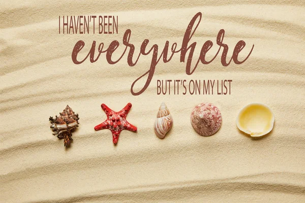 Puesta plana de conchas marinas y estrellas de mar rojas en la playa de arena en verano con no he estado en todas partes, pero está en mi lista de dejar - foto de stock