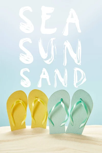 Summer yellow and blue flip flops in golden sand isolated on blue with sea, sun and sand lettering — Stock Photo