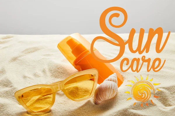 Yellow stylish sunglasses and sunscreen in orange bottle on sand with seashell on grey background with sun care lettering — Stock Photo