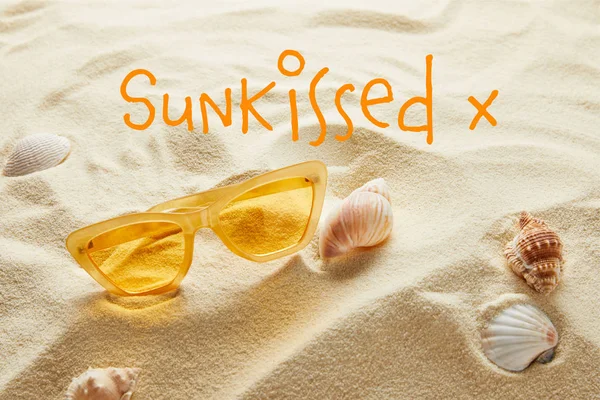 Occhiali da sole gialli eleganti su sabbia con conchiglie e scritte baciate dal sole — Foto stock