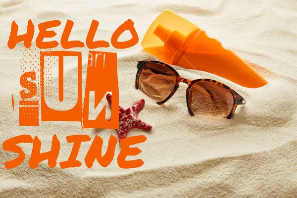 Brown stylish sunglasses and sunscreen in orange bottle on sand with hello sunshine lettering — Stock Photo