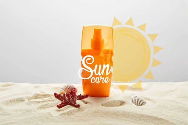 Солнцезащитный крем в оранжевой бутылке на песке с морской звездой на сером фоне с надписью — стоковое фото