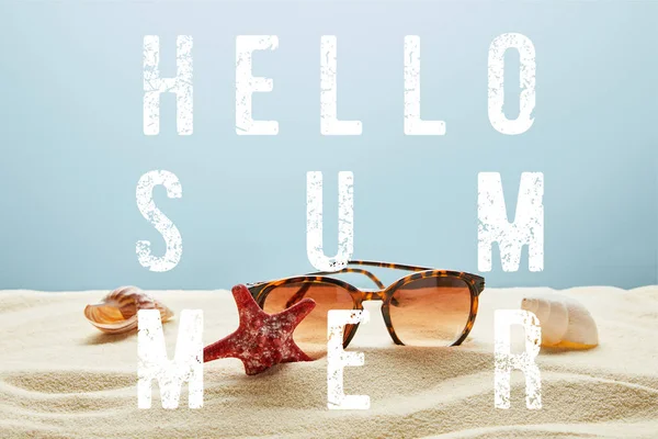 Gafas de sol con estilo marrón sobre arena con conchas marinas y estrellas de mar sobre fondo azul con letras de hola verano - foto de stock