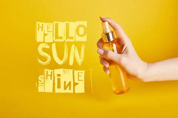 Cropped view of woman holding bottle with sunscreen spray on yellow background with hello sunshine lettering — Stock Photo