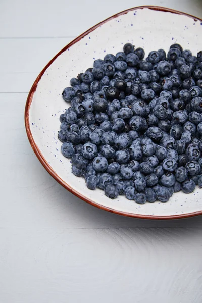 Assiette avec de délicieux bleuets sur table en bois blanc — Photo de stock