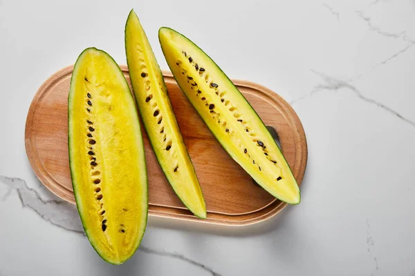 Draufsicht auf geschnittene köstliche exotische gelbe Wassermelone mit Samen auf hölzernem Schneidebrett auf Marmoroberfläche — Stockfoto