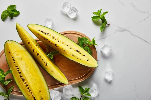 Top view of cut exotic yellow watermelon with seeds on marble surface with mint, ice and wooden chopping board — Stock Photo