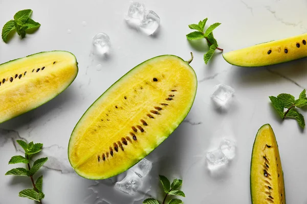 Draufsicht auf geschnittene köstliche exotische gelbe Wassermelone mit Samen auf Marmoroberfläche mit Minze, Eis — Stockfoto