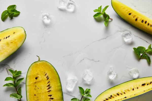 Draufsicht auf geschnittene köstliche exotische gelbe Wassermelone mit Samen auf Marmoroberfläche mit Minze, Eis und Kopierraum — Stockfoto