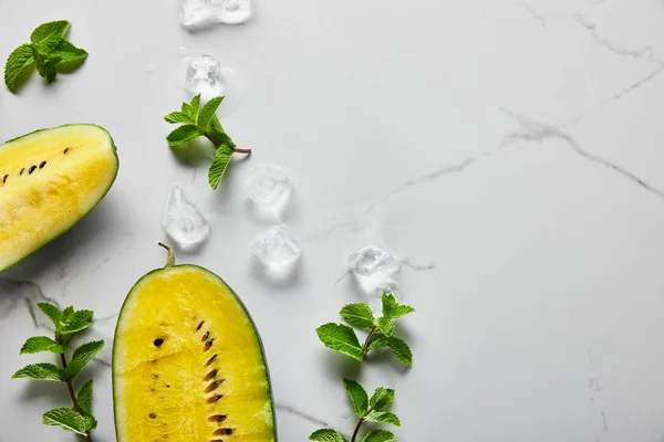 Vue de dessus de délicieux melon d'eau jaune exotique coupé avec des graines sur la surface de marbre avec menthe et glace — Photo de stock