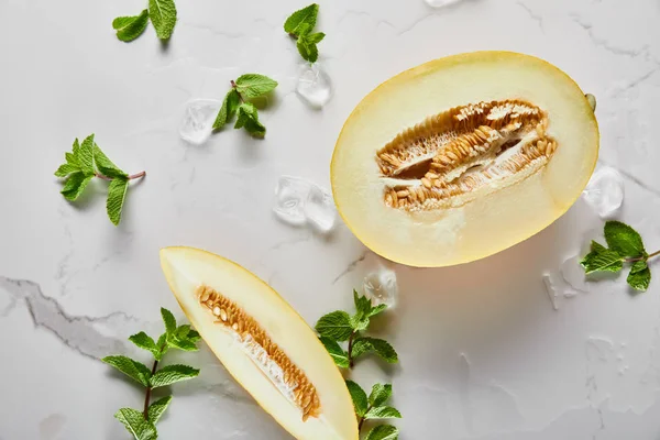 Vista superior de corte delicioso melón con semillas en la superficie de mármol con menta y hielo - foto de stock