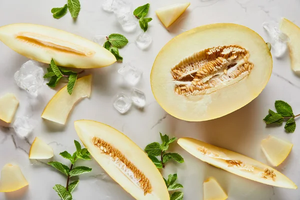 Vista superior de corte delicioso melón de temporada en la superficie de mármol con menta y hielo - foto de stock