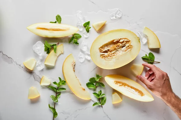 Vue de dessus du melon délicieux coupé sur la surface de marbre avec menthe et glace près de la main de l'homme — Photo de stock