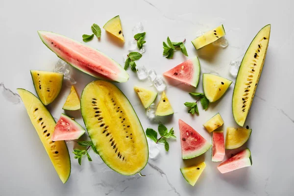 Draufsicht auf geschnittene köstliche exotische gelbe und rote Wassermelonen mit Eis und Minze auf Marmoroberfläche — Stockfoto