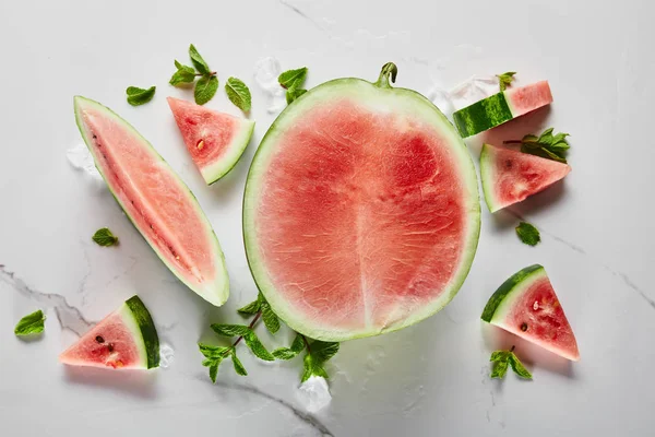 Draufsicht auf geschnittene köstliche exotische rote Wassermelone mit Samen auf Marmoroberfläche mit Eis und Minze — Stockfoto