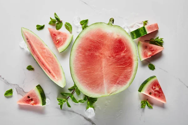 Vue de dessus de délicieux melon d'eau rouge exotique coupé avec des graines sur la surface de marbre avec de la glace et de la menthe — Photo de stock