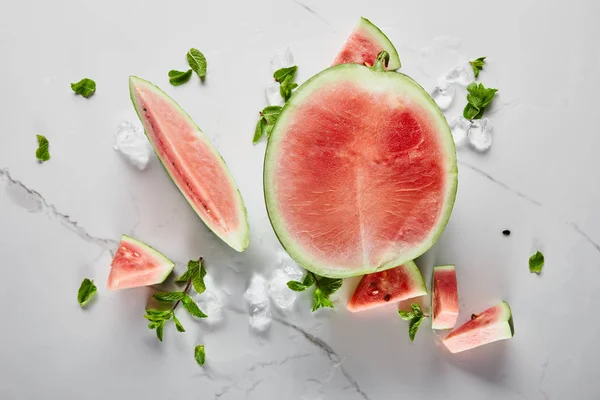 Draufsicht auf geschnittene köstliche rote Wassermelone mit Samen auf Marmoroberfläche mit Eis und Minze — Stockfoto