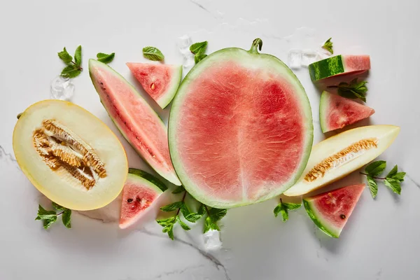 Draufsicht auf geschnittene köstliche exotische rote Wassermelone mit Melone auf Marmoroberfläche mit Eis und Minze — Stockfoto