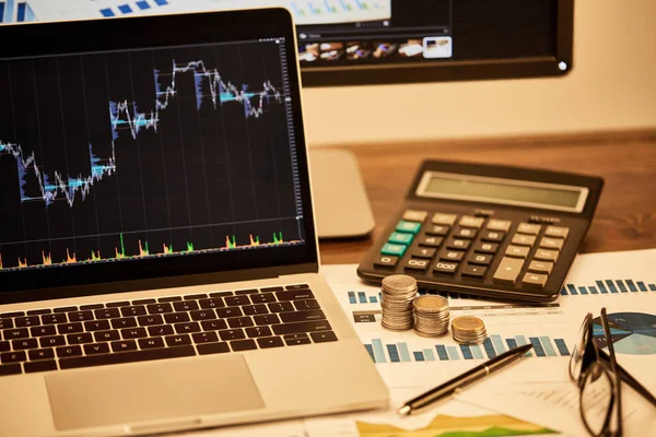 Laptop with graphs, coins, papers, pen, glasses and calculator — Stock Photo