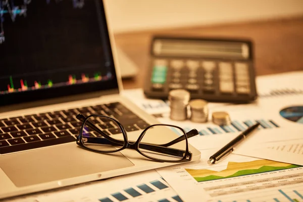 Enfoque selectivo de la computadora portátil, monedas, papeles, gafas, pluma y calculadora en la mesa - foto de stock