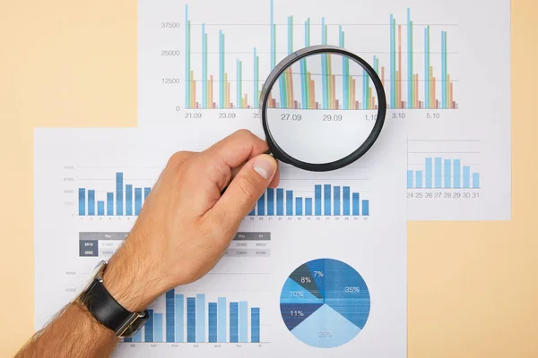 Cropped view of man holding magnifying glass and looking at papers — Stock Photo