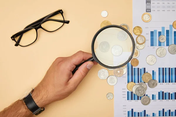 Cropped view of man holding magnifying glass and looking at coins — Stock Photo