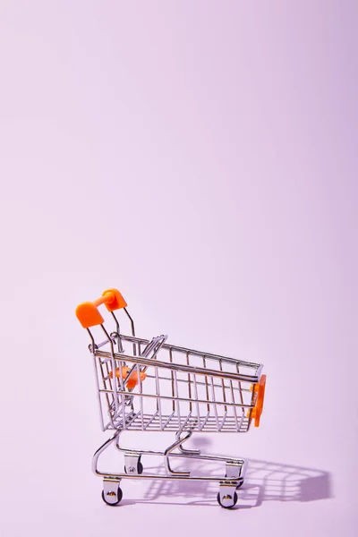 Pequeño carrito de compras decorativo sobre fondo violeta - foto de stock