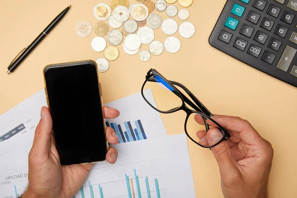 Vista recortada del hombre adulto sosteniendo gafas y teléfono inteligente en la oficina - foto de stock