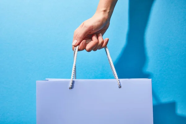 Vista cortada de mulher segurando saco de compras roxo no azul — Fotografia de Stock
