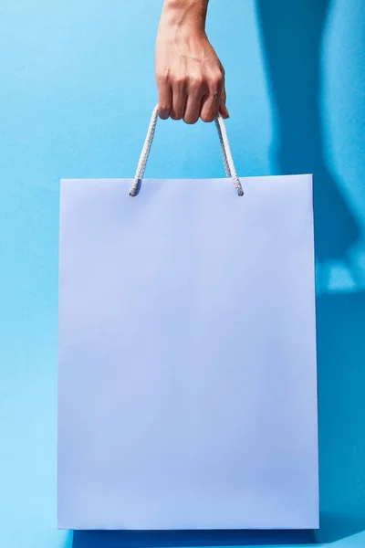 Vista recortada de la mujer sosteniendo bolso de compras púrpura sobre fondo azul - foto de stock