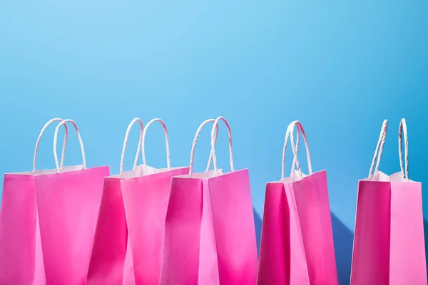 Quelques sacs à provisions en papier rose avec poignées blanches sur fond bleu — Photo de stock