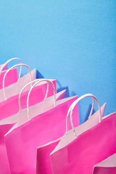 Sacos de compras de papel rosa com alças brancas no fundo azul — Fotografia de Stock