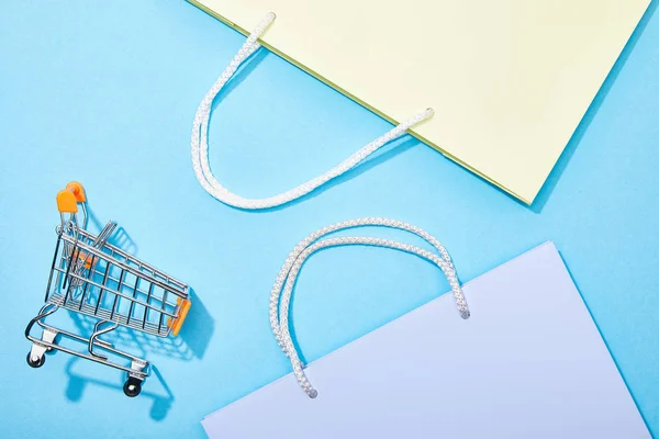 Vista superior de las bolsas de compras cerca del carrito de compras de juguete en azul - foto de stock