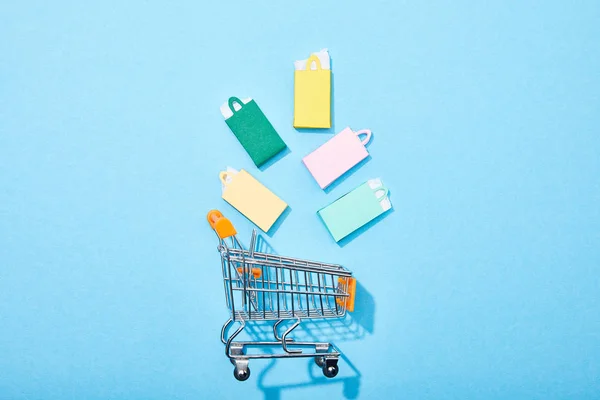 Vue du dessus des sacs en papier colorés tombant dans le panier de jouets sur bleu — Photo de stock