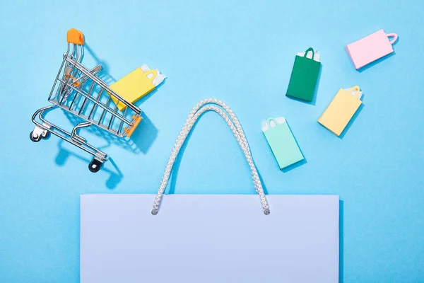 Vue du dessus du panier de jouets et des sacs en papier colorés tombant dans le sac à provisions violet sur bleu — Photo de stock