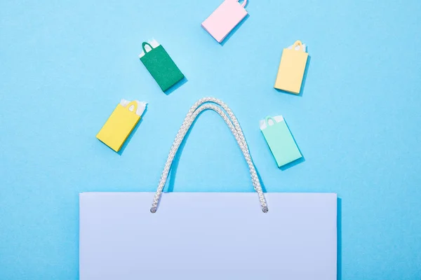 Вид зверху барвисті паперові мішки, що падають у фіолетовий сумку для покупок на синьому — стокове фото