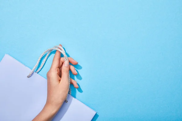 Cropped view of woman holding shopping bag on blue background — Stock Photo