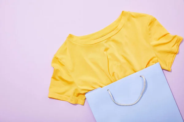 Top view of yellow t-shirt in purple shopping bag on violet — Stock Photo