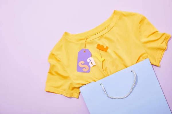 Vue du dessus du lettrage de vente sur t-shirt jaune avec étiquette en papier violet dans un sac à provisions violet — Photo de stock