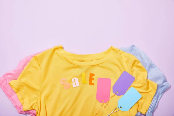 Top view of sale lettering on t-shirts with colorful tags on violet — Stock Photo