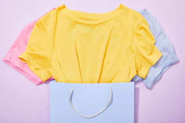 Vue du dessus de t-shirts colorés dans un sac à provisions sur violet — Photo de stock