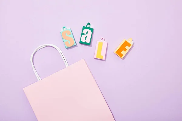 Vista dall'alto di borse giocattolo con iscrizione in vendita vicino alla shopping bag rosa su viola — Foto stock