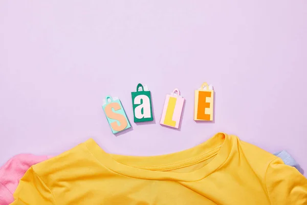 Vista dall'alto di colorate borse giocattolo con scritte in vendita vicino a t-shirt su viola — Foto stock