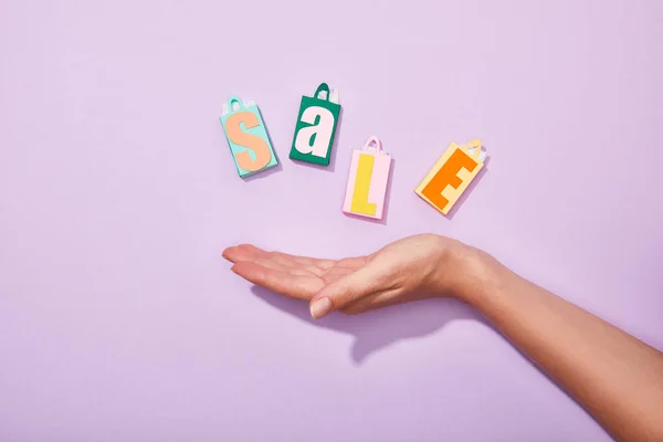 Vista cortada da mão da mulher perto de sacos de papel coloridos com lettering venda em violeta — Fotografia de Stock