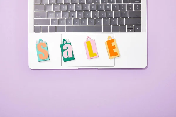 Top view of colorful toy shopping bags with sale lettering on laptop on violet — Stock Photo