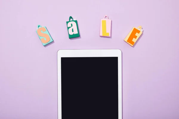 Вид зверху паперові сумки з розпродажем біля цифрового планшета з порожнім екраном на фіолетовому — стокове фото