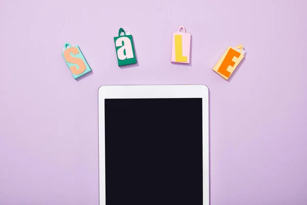 Top view of paper shopping bags with sale lettering near digital tablet with blank screen on violet — Stock Photo