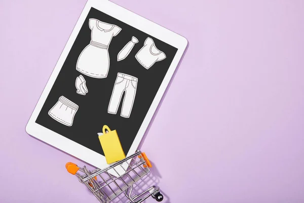 Vue du dessus de la coupe de papier des vêtements sur tablette numérique tombant dans le panier de jouets sur violet, concept e-shopping — Photo de stock